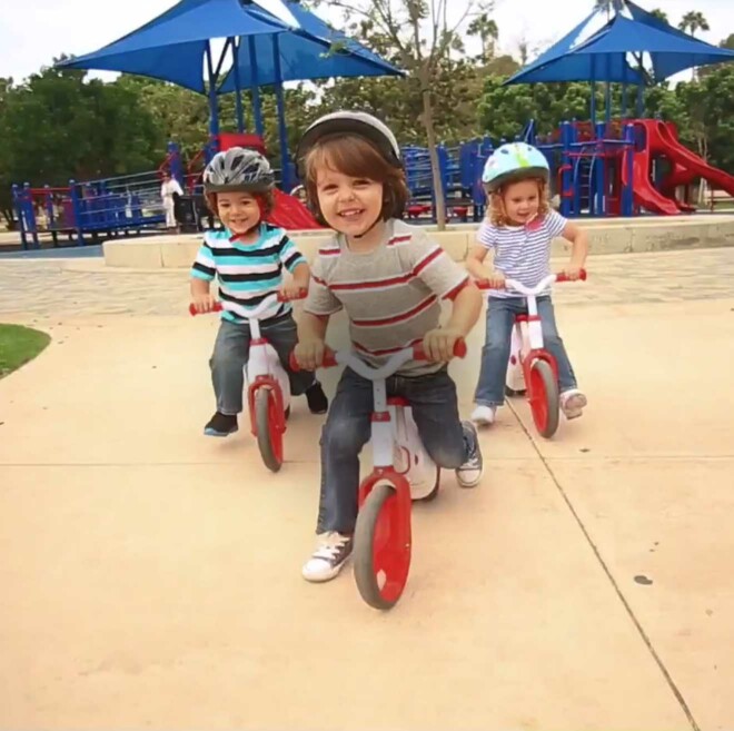 Three kids with smiles riding Velo Twista Balance Bikes.