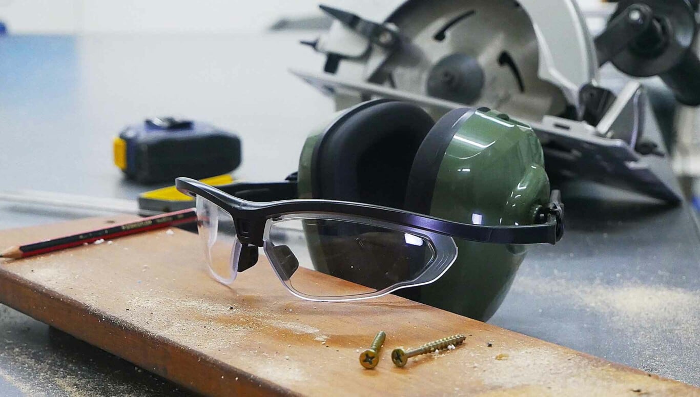 Eyesonic sitting on wooden plank on work bench with tools.