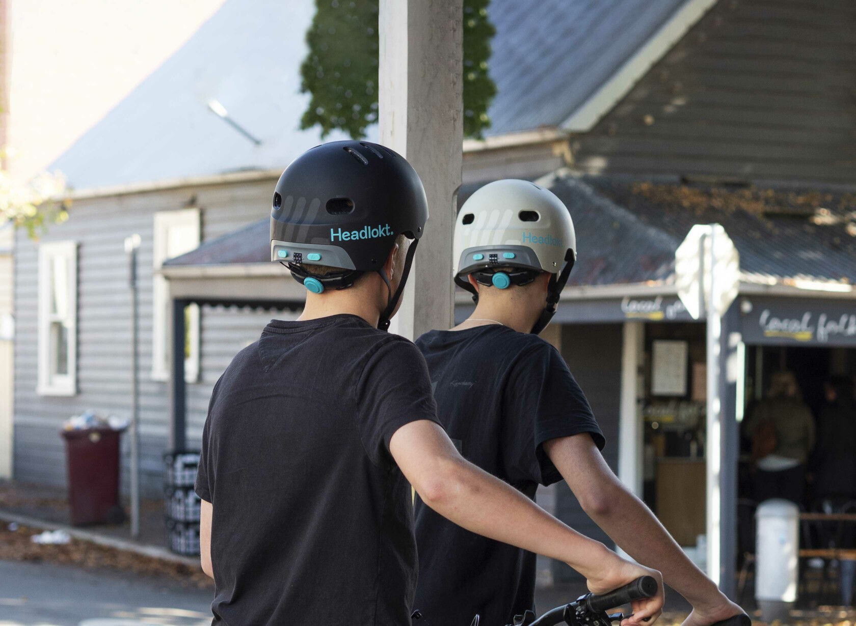 Two boys wearing Headlokt bike helmets leaning against bike, facing away.